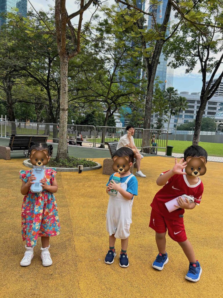 3 kids standing and holding their bottles drinking water at the KLCC park playground 