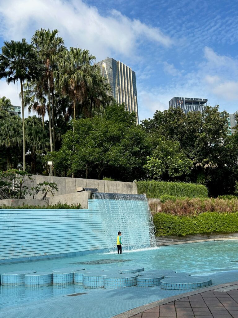 a young boy standing underneath a small waterfall at the KLCC Park wading pool