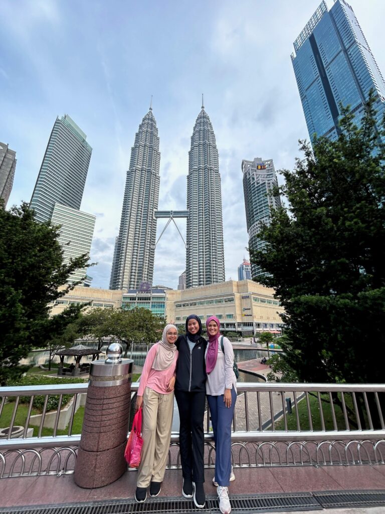 three friends standing on top of a bridge at KLCC Park with the KLCC Petronas Twin Towers in the background 