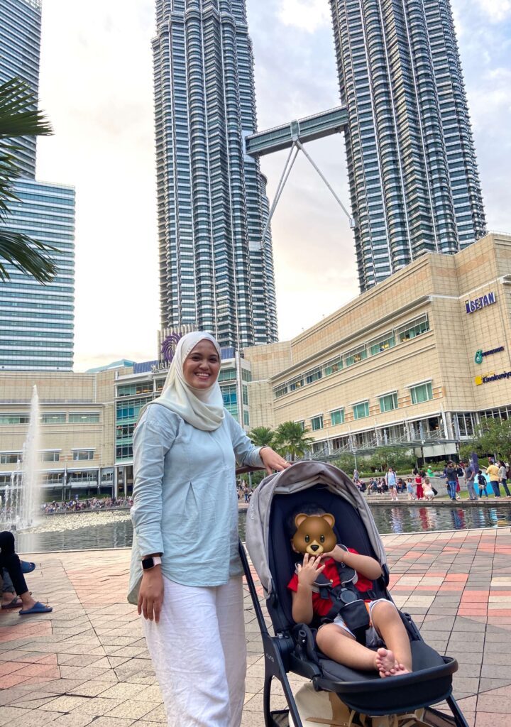 woman with her baby in stroller standing in front of symphone lake at KLCC park 