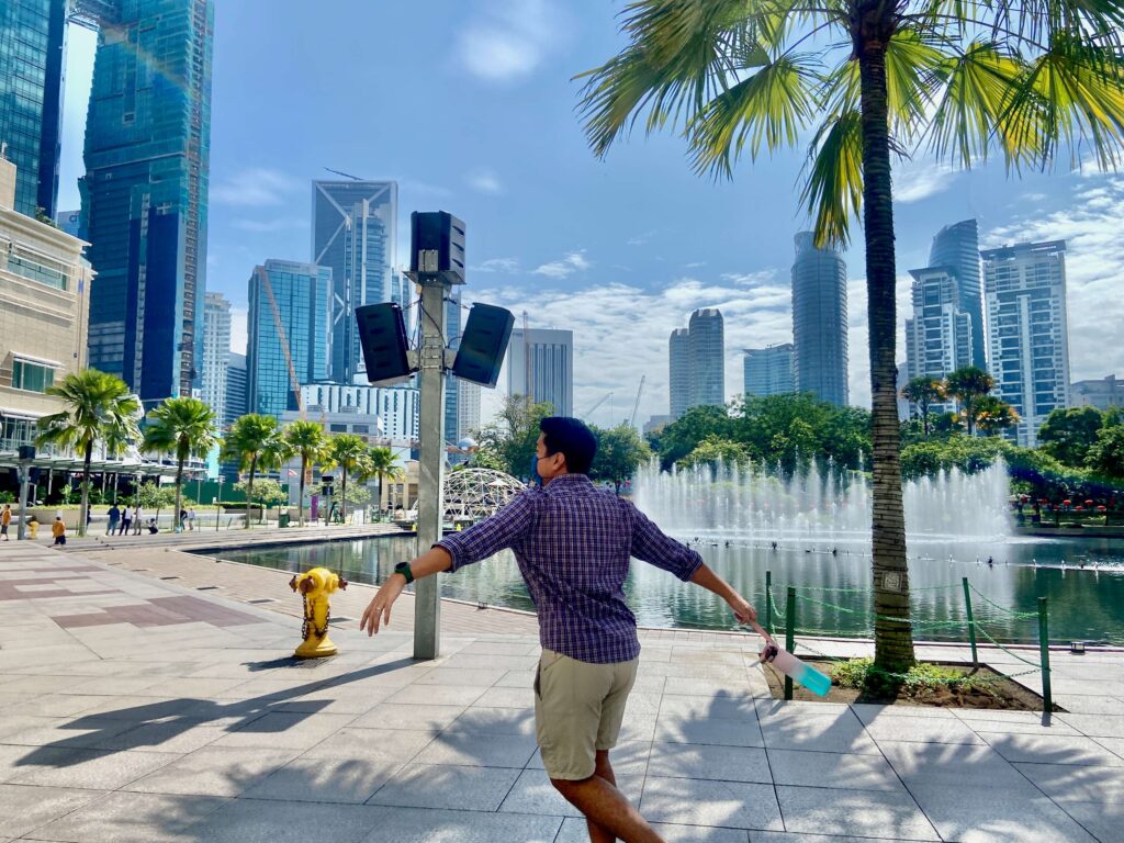 man with his arms up in front of the symphony lake at klcc park