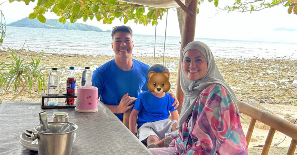 A couple with their son sitting by a dining table by with the Patong beach in Phuket in the background