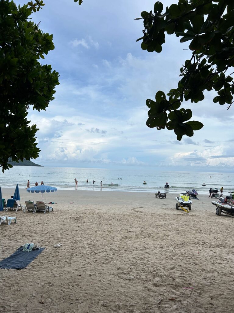 Kata Beach with soft sand and water with rolling clouds, people swimming in the water 