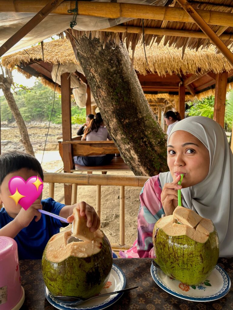 Woman and son sipping coconut water from coconut by the beach in Phuket